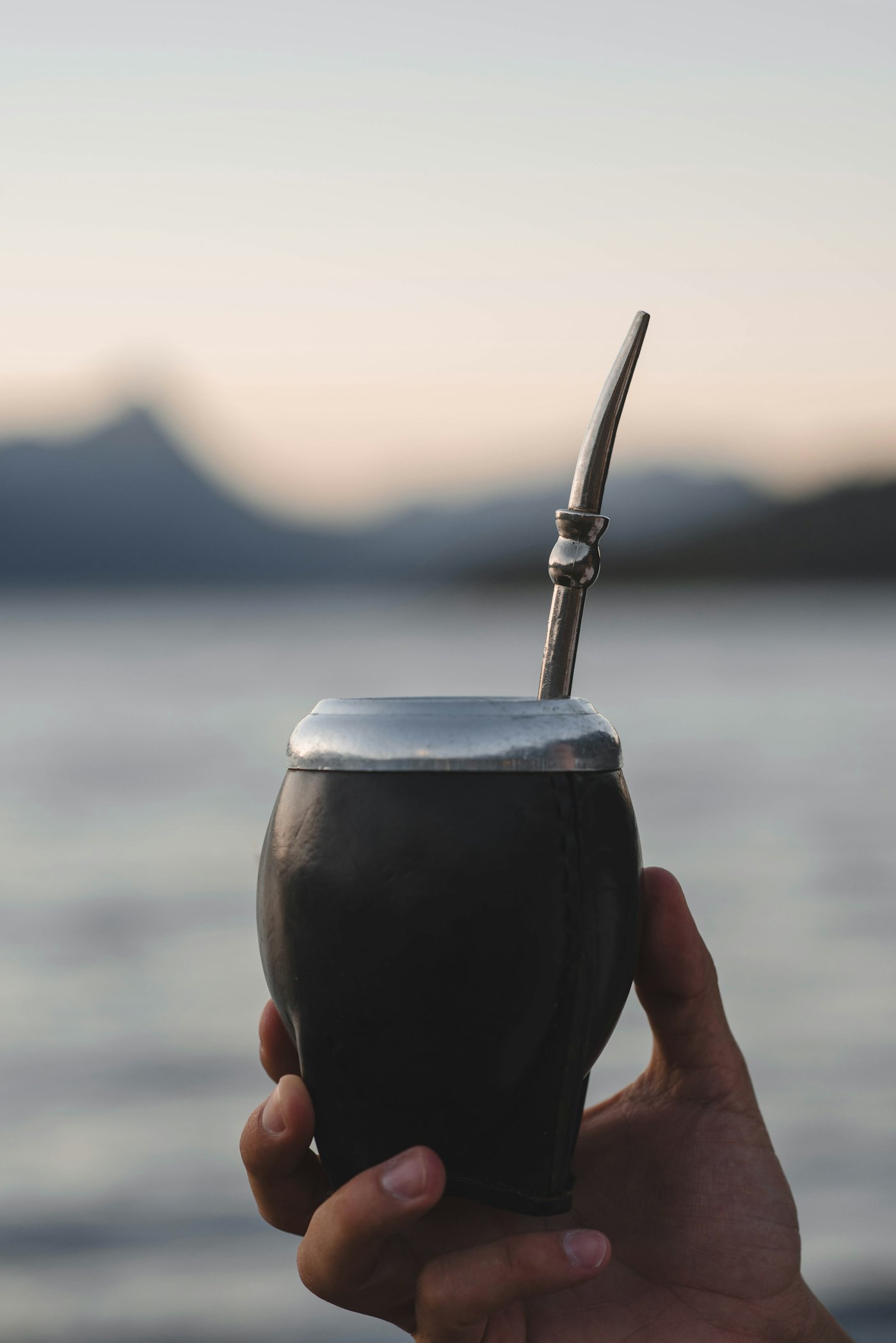 A hand holding a mate gourd by a lake